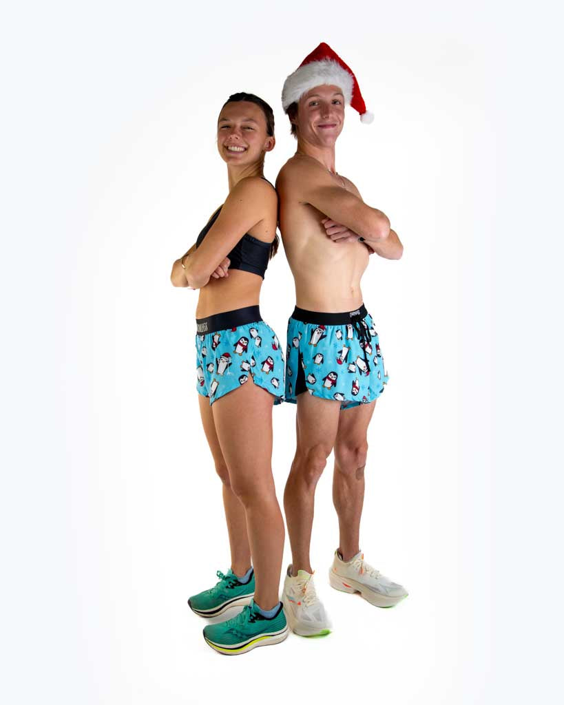 Full body view of models wearing ChicknLegs Men’s 2-inch DS Split Running Shorts featuring a soft elastic drawstring waistband, inner pocket, and black mesh liner for full coverage and breathability and the women's 1.5 inch split running shorts, featured in the slippery bois penguin design with santa hats.