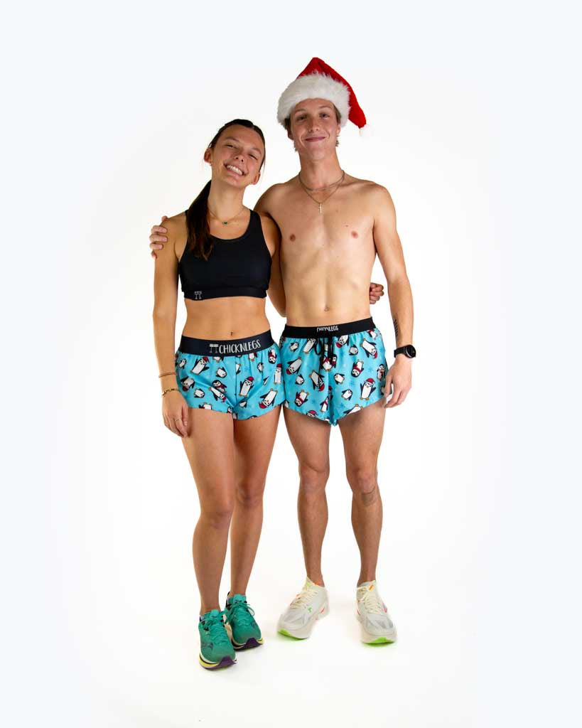 Full body view of models wearing ChicknLegs Men’s 2-inch DS Split Running Shorts featuring a soft elastic drawstring waistband, inner pocket, and black mesh liner for full coverage and breathability and the women's 1.5 inch split running shorts, featured in the slippery bois penguin design with santa hats.