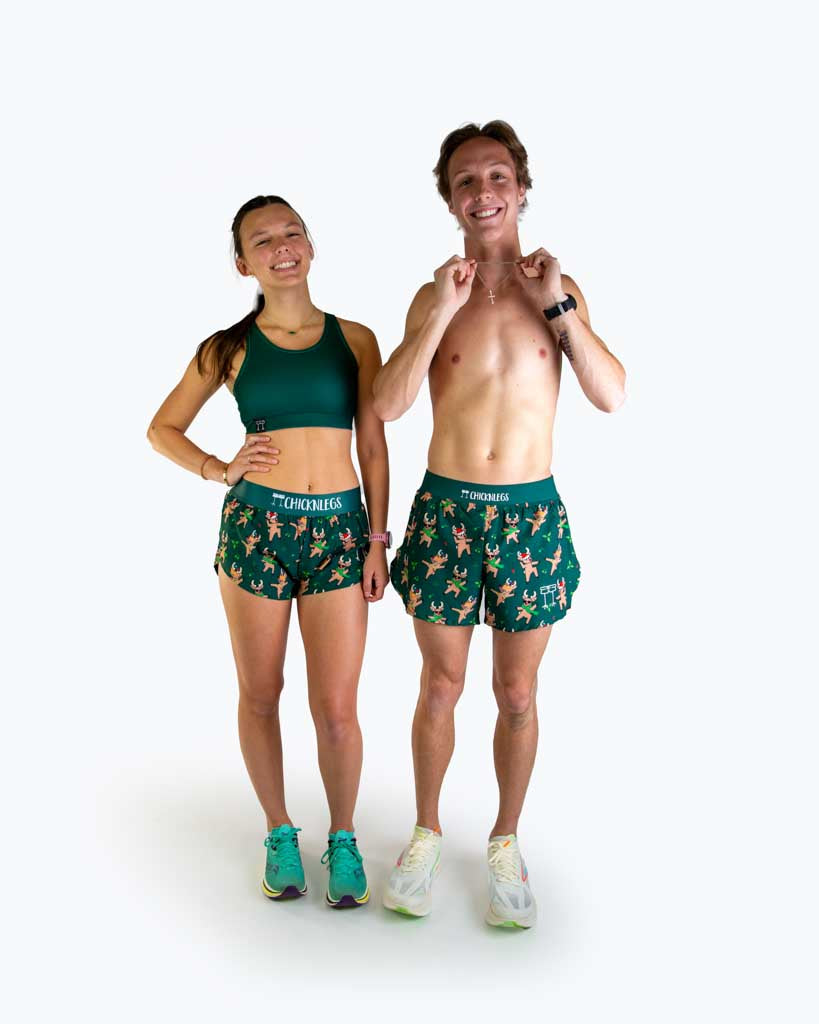 Full body view of models wearing ChicknLegs men’s 4-inch split running shorts featuring a soft elastic waistband, rear zipper pocket, and black mesh liner for full coverage and breathability and women's 1.5 inch split running shorts in the rockin reindeer design with a dark green background.