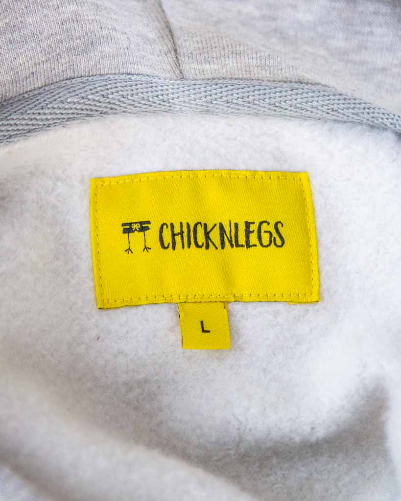 Close up view of ChicknLeg's Varsity Oversized Unisex Hoodie's hemtag in yellow.