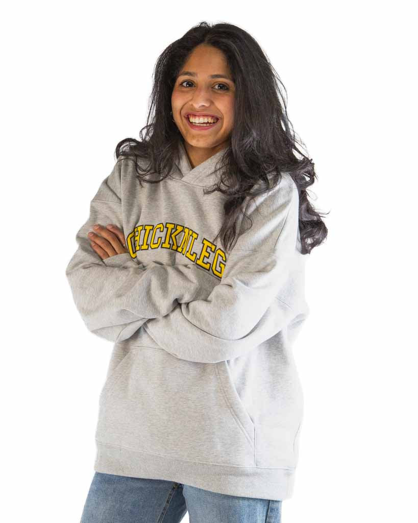 Women model is wearing ChicknLegs in the Varsity Oversized Unisex Hoodie featuring midweight fabric, loose relaxed fit, and embroidered front logo.