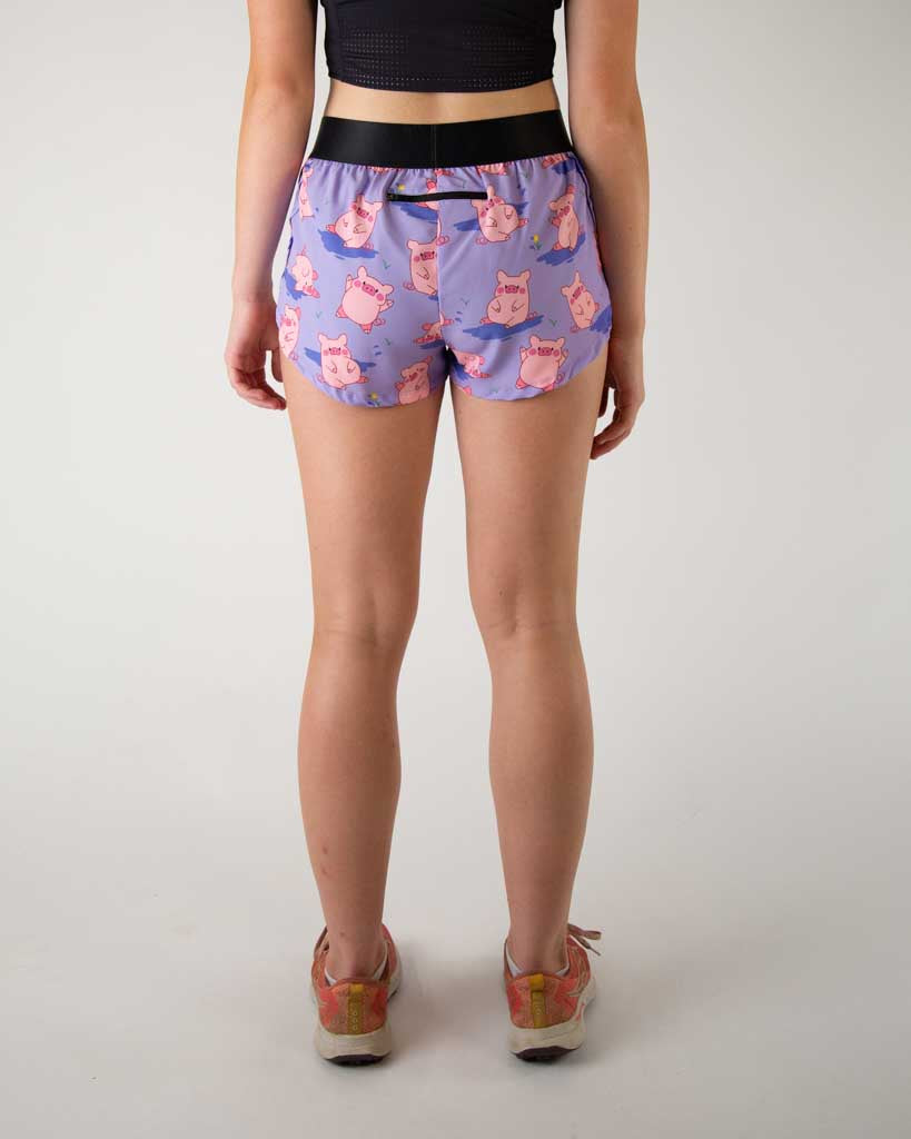 Back side view of ChicknLegs women’s 1.5-inch split running shorts with drawstring, breathable liner, lilac purple background and pink piggies design. A pocket is shown on the back.