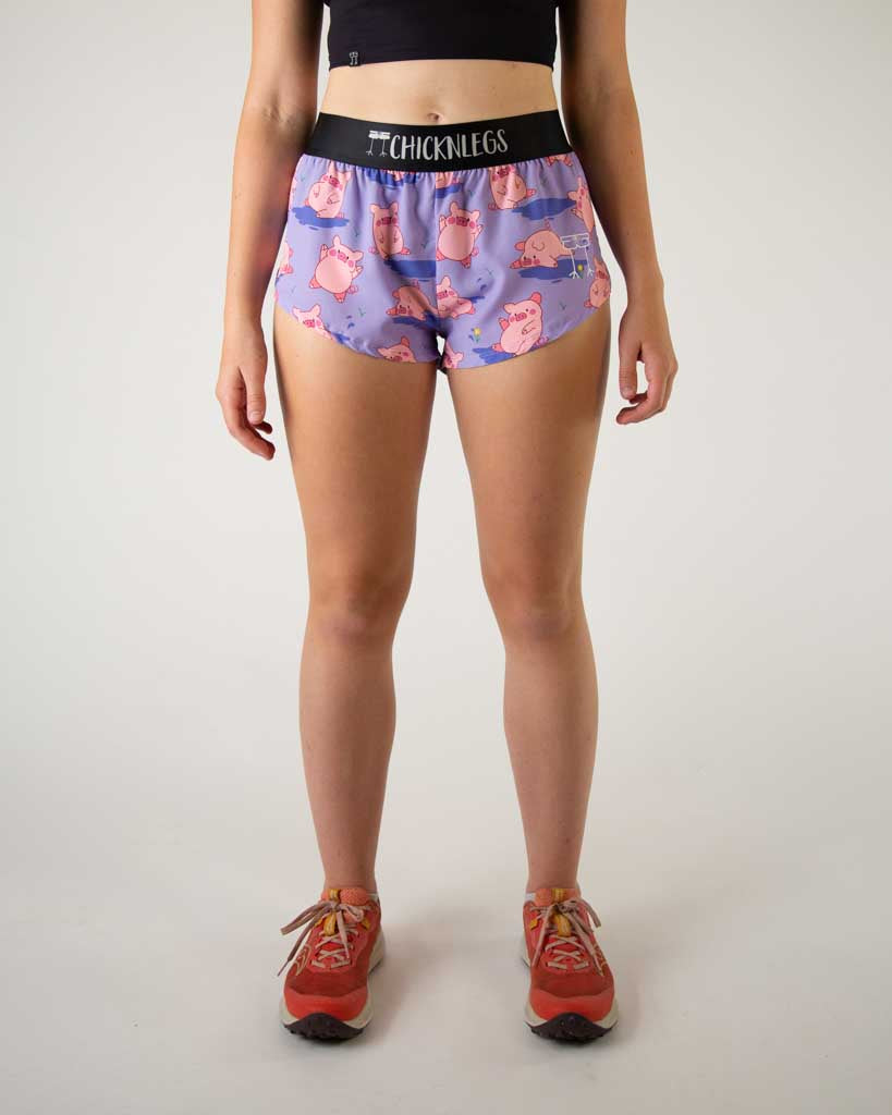 Front image of ChicknLegs women’s 1.5-inch split running shorts with drawstring, breathable liner, lilac purple background and pink piggies design.
