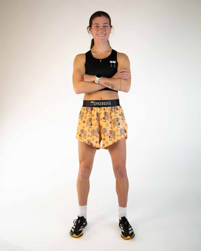 Full body view of model wearing ChicknLegs Women’s 4-inch split running shorts in the Pardoned Turkey design, great for Thanksgiving and Turkey Trot runs that features soft elastic waistband, 3-inch side split, rear zipper pocket, and black mesh liner for breathability and coverage.