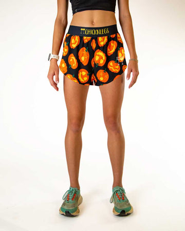 Runner is wearing ChicknLegs in the women's 4 inch split running shorts in the Pumpkin design. This print has orange jack o lanterns with a black background and black waistband to match.