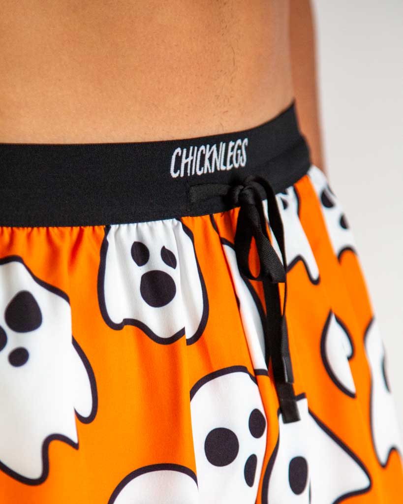 Close-up detail of ChicknLegs men’s 2-inch running shorts, orange fabric with halloween ghost pattern and drawstring waistband.