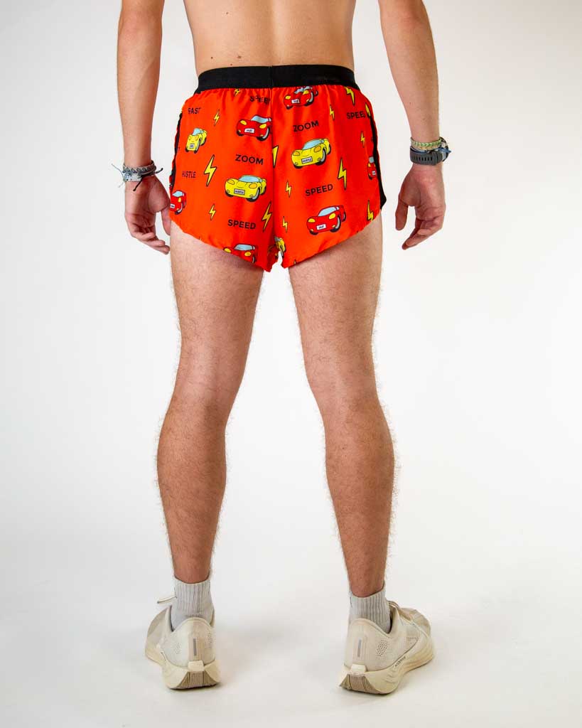 Back view of ChicknLegs men’s 2-inch split running shorts in red orange with yellow lightning bolt pattern, red and yellow cars, and showing elastic waistband with breathable liner.