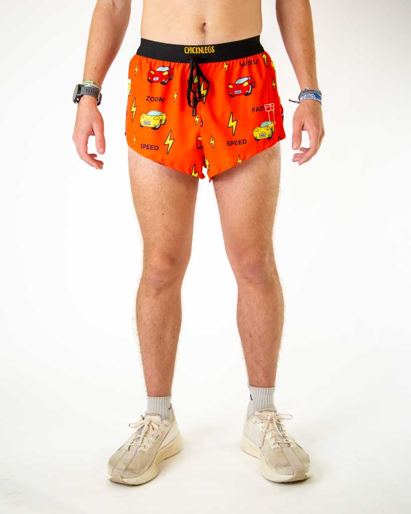 Front view of ChicknLegs men’s 2-inch split running shorts with drawstring, breathable liner, red orange background and yellow lightning bolt design with red and yellow cars.