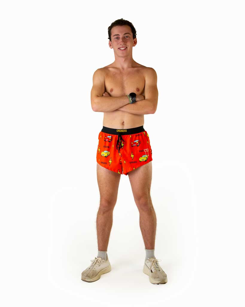 Full body view of model wearing ChicknLegs men’s 2-inch split running shorts in the cars design, showing red and yellow cars, lightning bolts for speed and black waistband with matching white shoes.