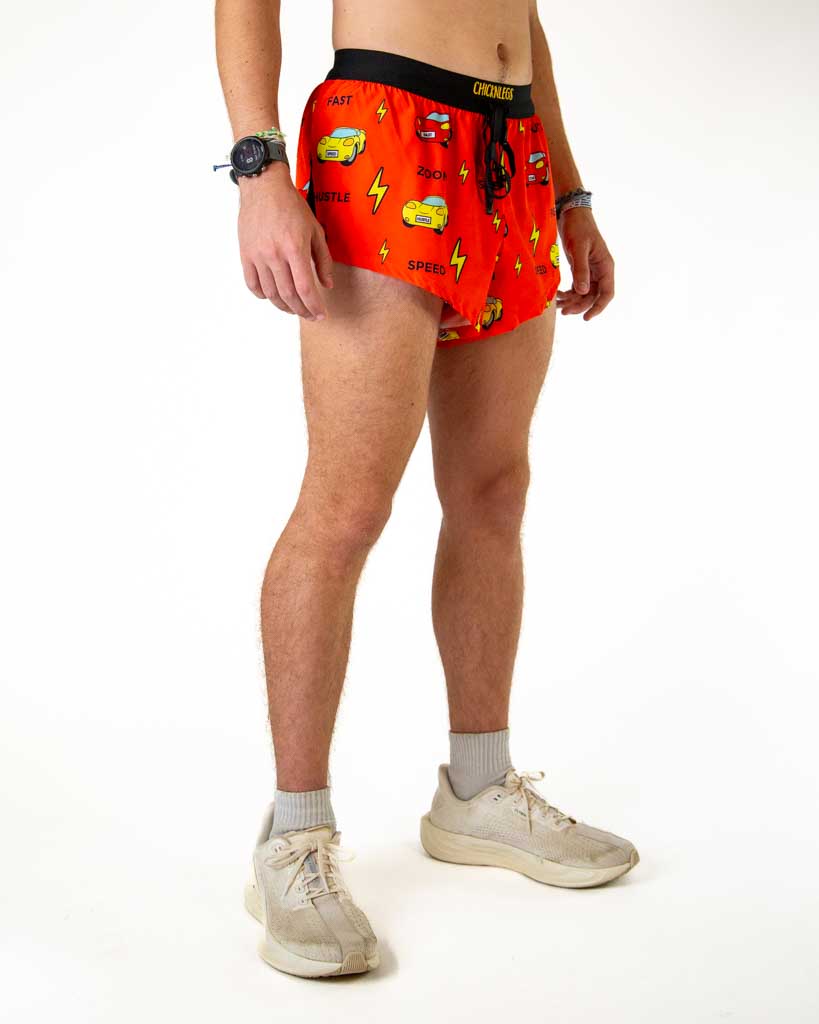 Right side view of ChicknLegs men’s 2-inch hot pink split running shorts with red orange background with cars and black waistband.