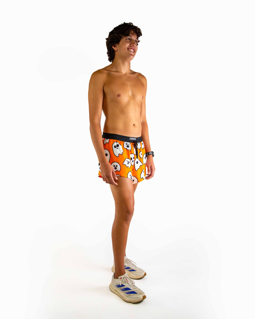 Full body view of model wearing ChicknLegs men’s 2-inch split running shorts in orange with the ghost design styled with white running shoes.