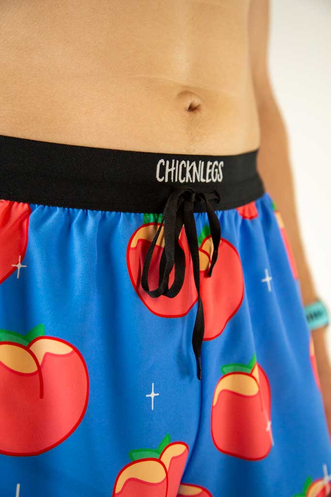 A close up view of ChicknLegs men’s 2-inch split running shorts with drawstring, breathable liner, blue background and juicy peaches design.