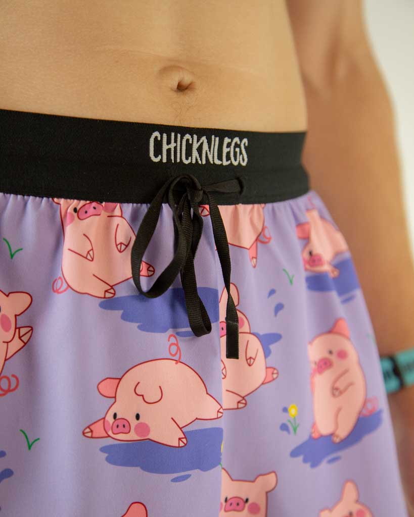 A close up view of ChicknLegs men’s 2-inch split running shorts with drawstring, breathable liner, lilac purple background and pink piggies design.