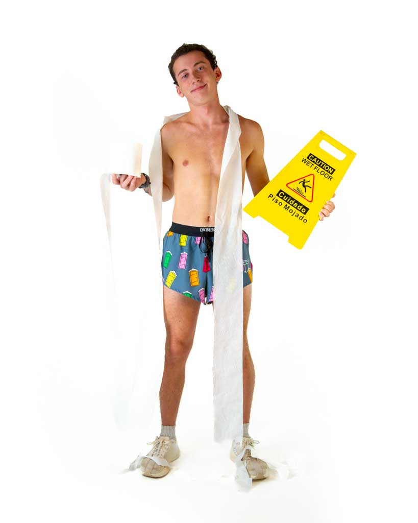 Full body view of model wearing ChicknLegs men’s 2-inch split running shorts in blue with porta pottys, styled with white running shoes and holding toilet paper.