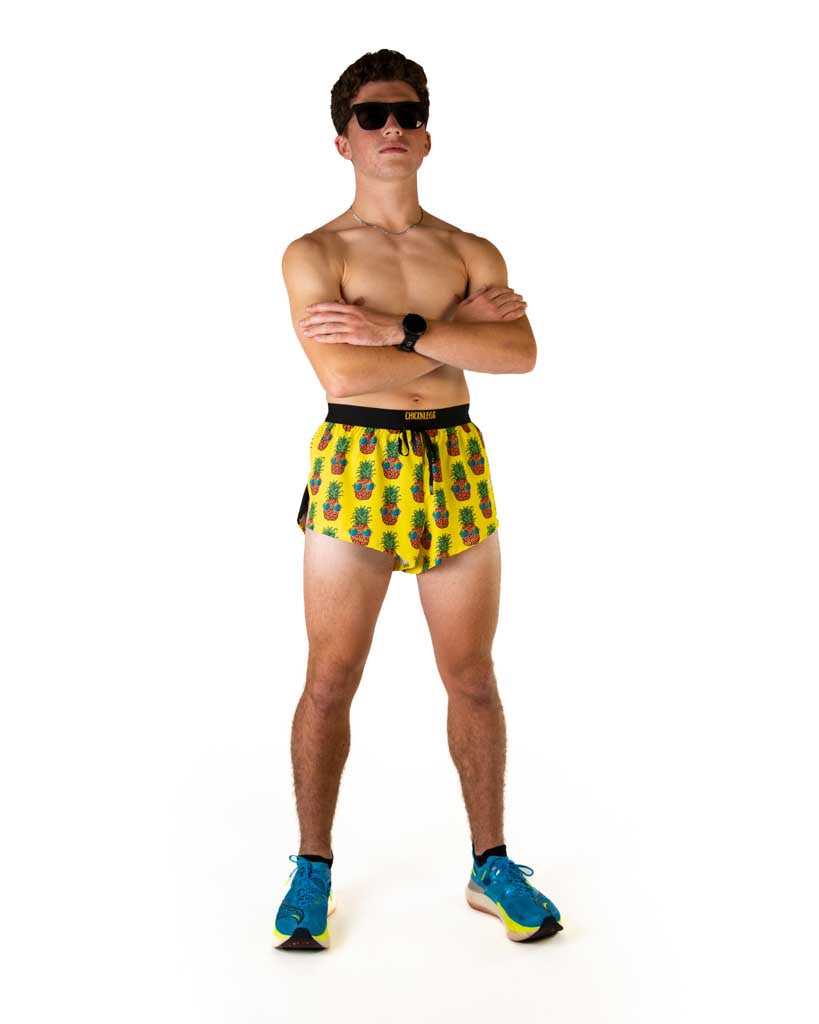 Full body view of model wearing ChicknLegs men’s 2-inch split running shorts in yellow with pineapples, styled with white blue running shoes.