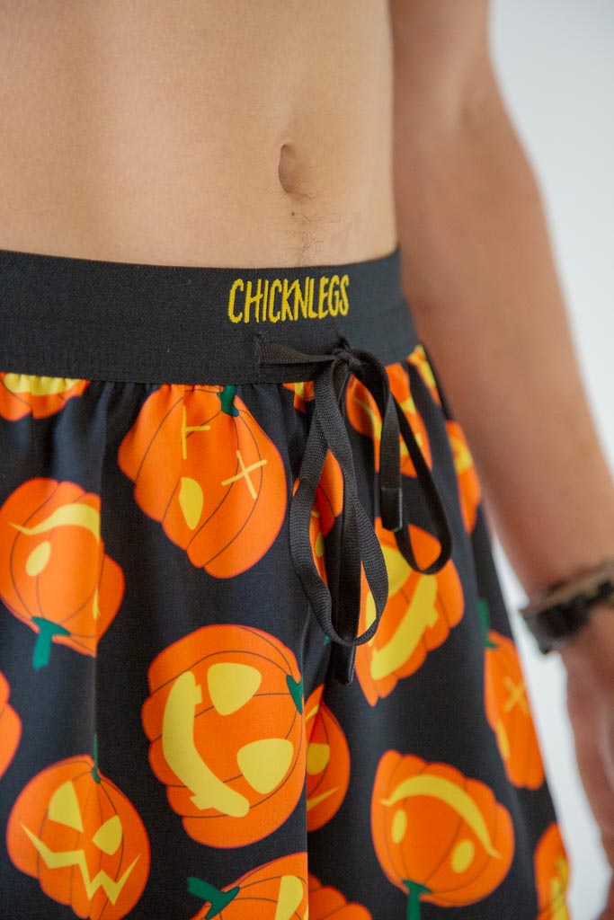 Close-up detail of ChicknLegs men’s 2-inch running shorts, black fabric background and orange pumpkin pattern and drawstring waistband.