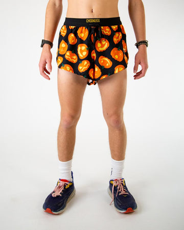 Front view of ChicknLegs men’s 2-inch split running shorts with drawstring, breathable liner, black background and orange pumpkin jack-o-lantern design.