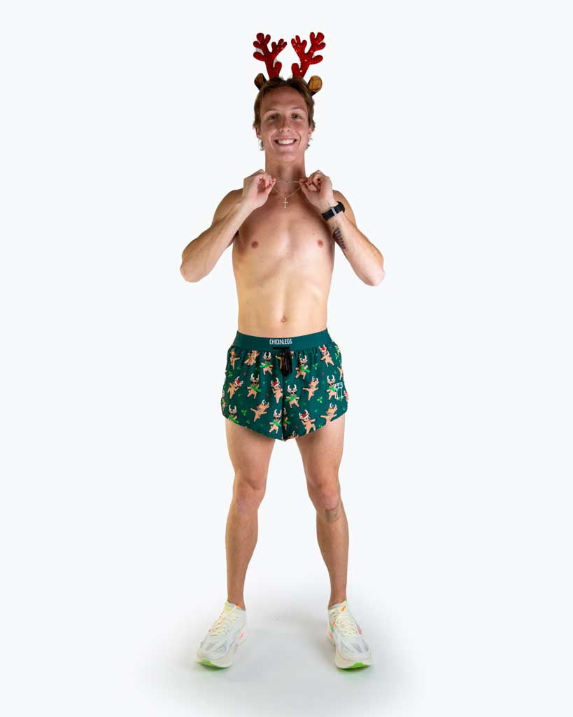 Full body view of model wearing ChicknLegs Men’s 2-inch DS Split Running Shorts featuring a soft elastic drawstring waistband, inner pocket, and black mesh liner for full coverage and breathability. Featured are the rockin reindeer design in christmas lights and santa hats with a dark green background.