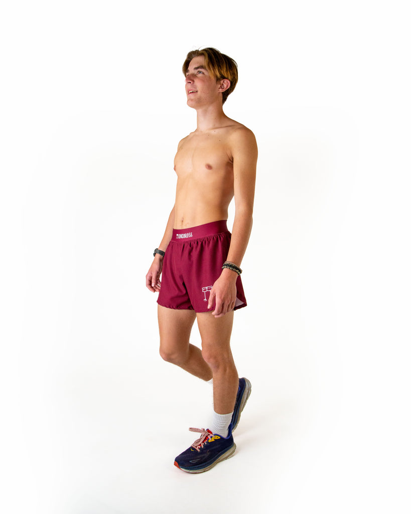 Full body view of model wearing ChicknLegs men’s 4-inch split running shorts in solid maroon, styled with black running shoes.