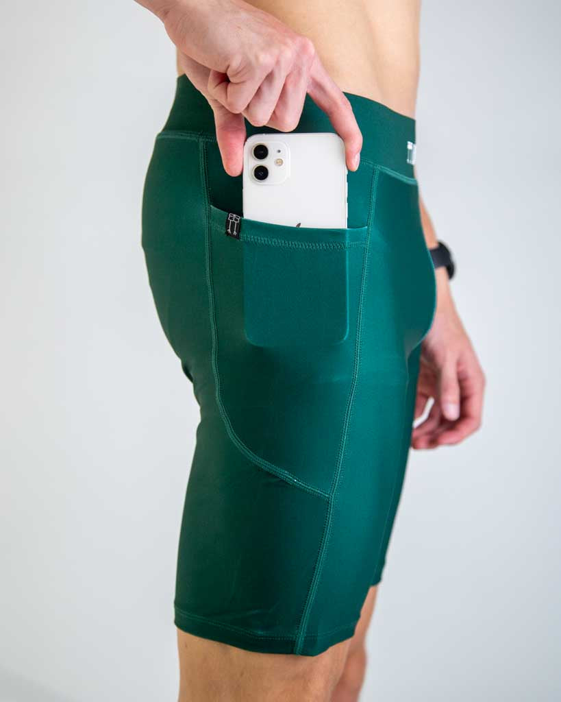 Close-up detail of ChicknLegs Men’s 8-inch Half Tights fabric and construction, featuring the soft elastic waistband, internal key pocket, and side pockets. Runner is placing phone into pocket to demonstrate the fit.