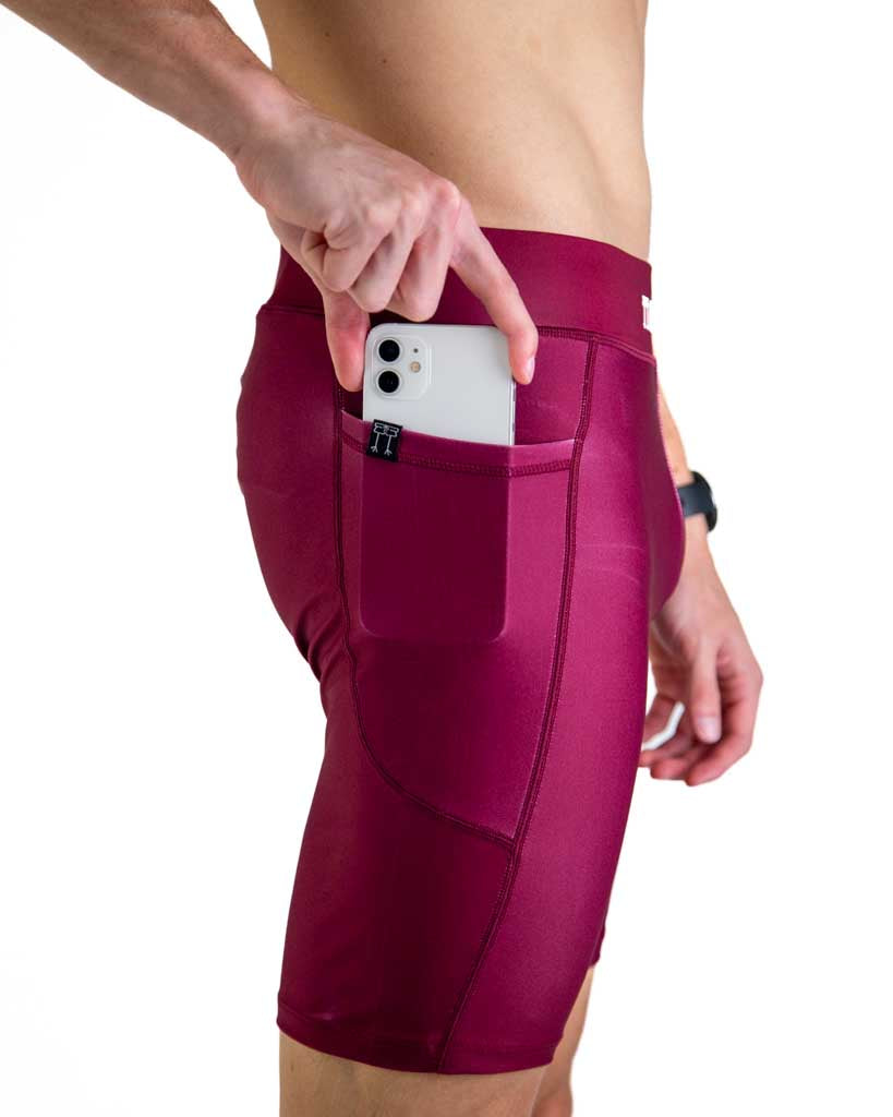 Close-up detail of ChicknLegs Men’s 8-inch Half Tights fabric and construction, featuring the soft elastic waistband and side pockets. Runner is placing phone into pocket to demonstrate the fit.