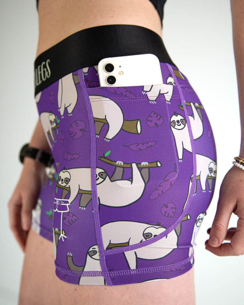 A close up view of ChicknLegs women’s 3-inch compression spandex running shorts with a purple background and sloths all over, showing side pockets and a phone being held inside.