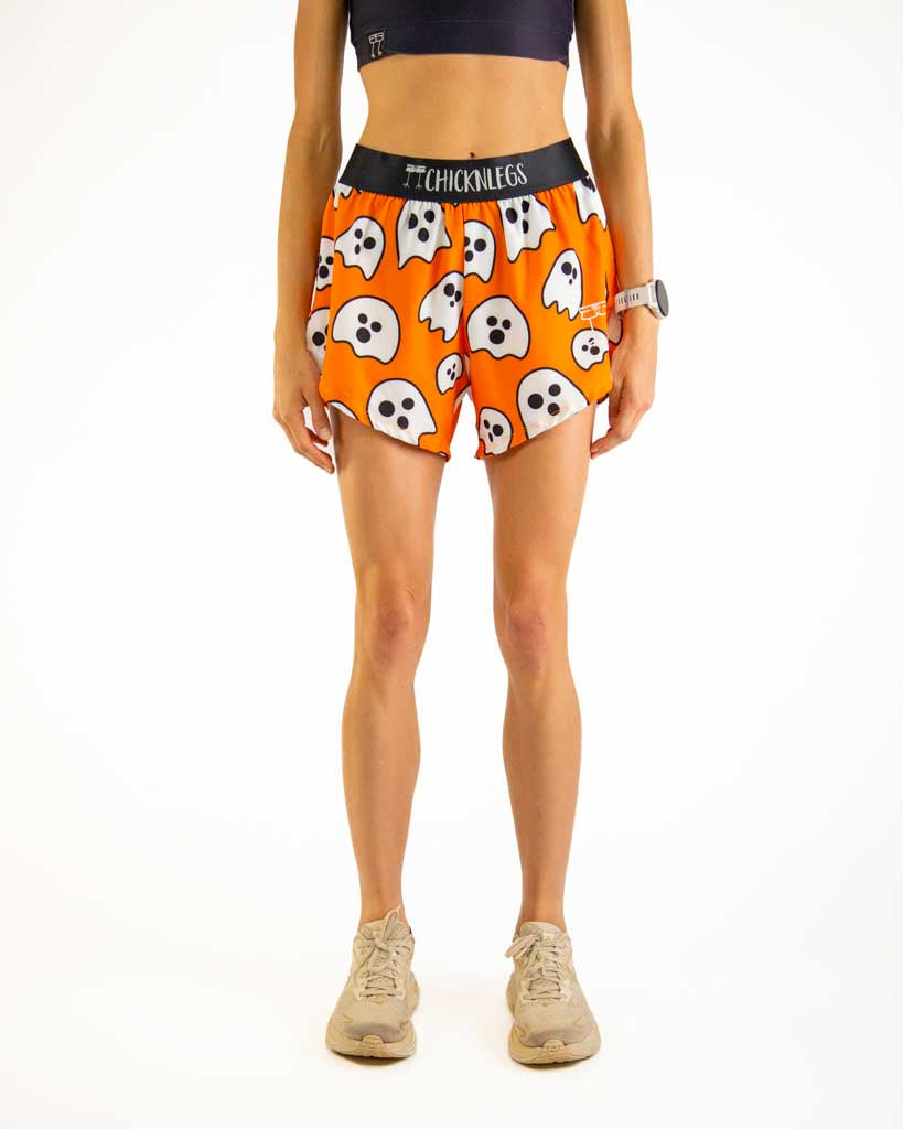Front view of ChicknLegs Women’s 4-inch split running shorts featuring a soft elastic waistband for a smooth, secure fit and black mesh liner for full coverage and breathability. Featured are the Ghost design, with orange background and black waistband.