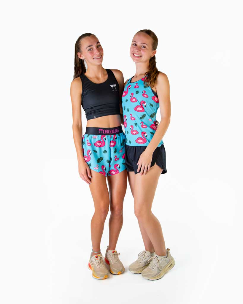 A full body image is shown of the runners wearing ChicknLegs black crop top and women's 4 inch split running shorts in the Blue Flamingo design, and the Blue Flamingo performance running singlet, matching with bright neon shoes.