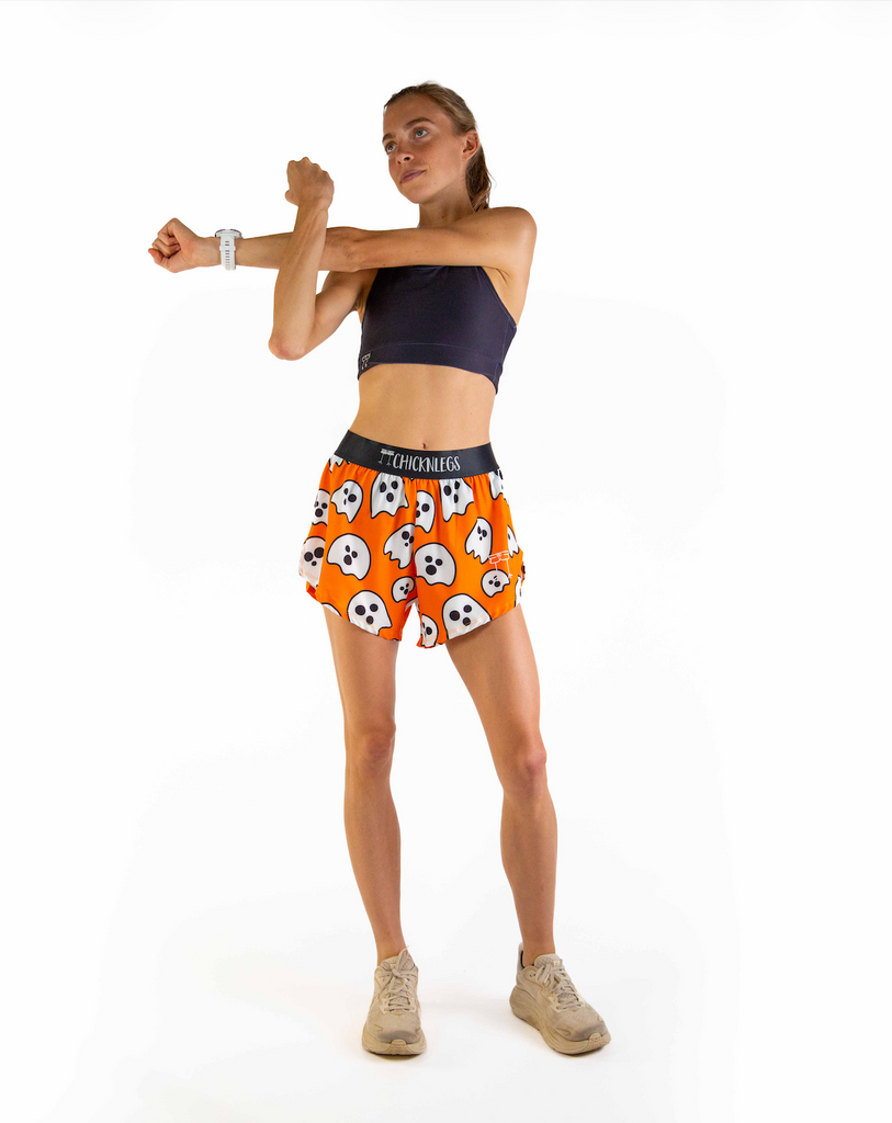 Full body view of model wearing ChicknLegs Women’s 4-inch split running shorts with soft elastic waistband, featured in the Ghost print with an orange background and matching black waistband.