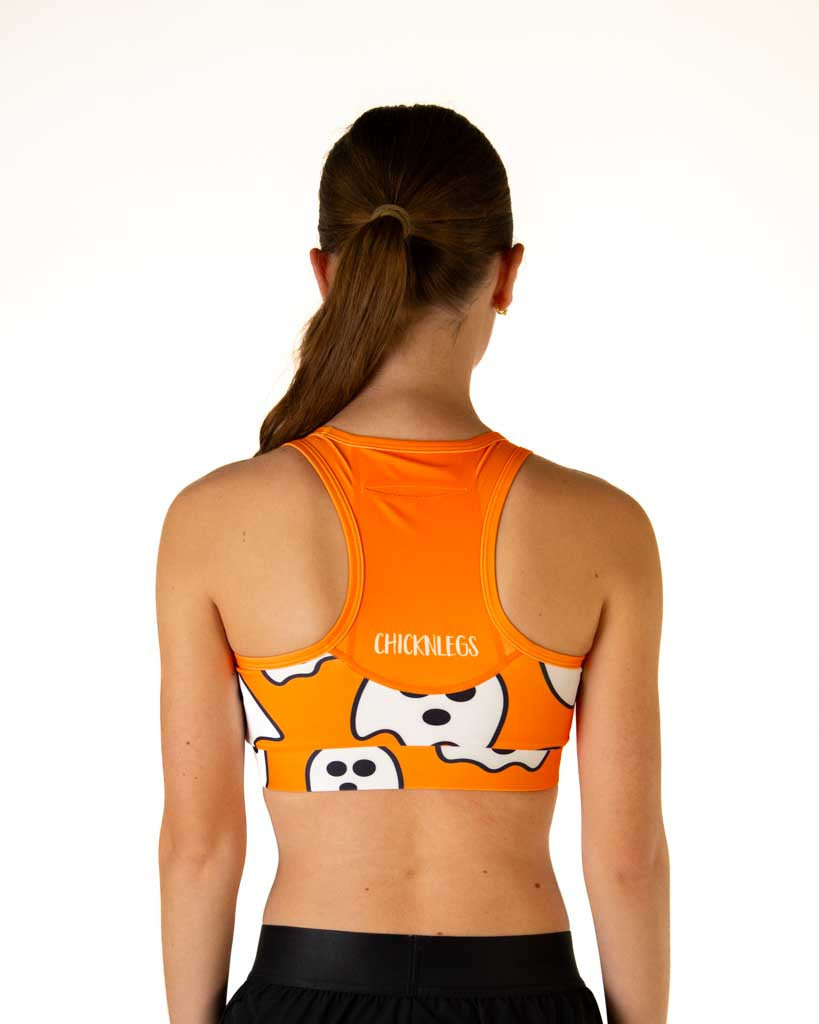 Back view of ChicknLegs women’s OG sports bra in orange with white ghosts, featuring built-in back pocket for storage and phones.