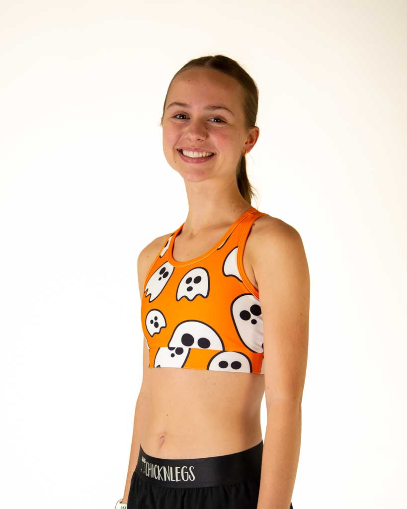 Left side view of runner wearing ChicknLegs OG Sports Bra with an orange background that is decorated with scattered Halloween ghost.