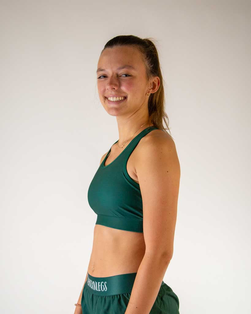 Left side view of ChicknLegs women’s OG sports bra in solid forest green, showing straps and supportive fit and coverage.