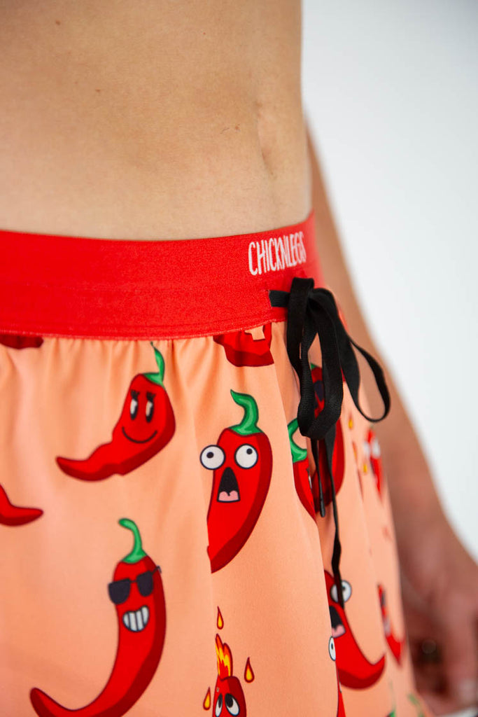 Close-up detail of ChicknLegs men’s 2-inch running shorts, orange fabric with red chili pepper pattern and drawstring with red waistband.