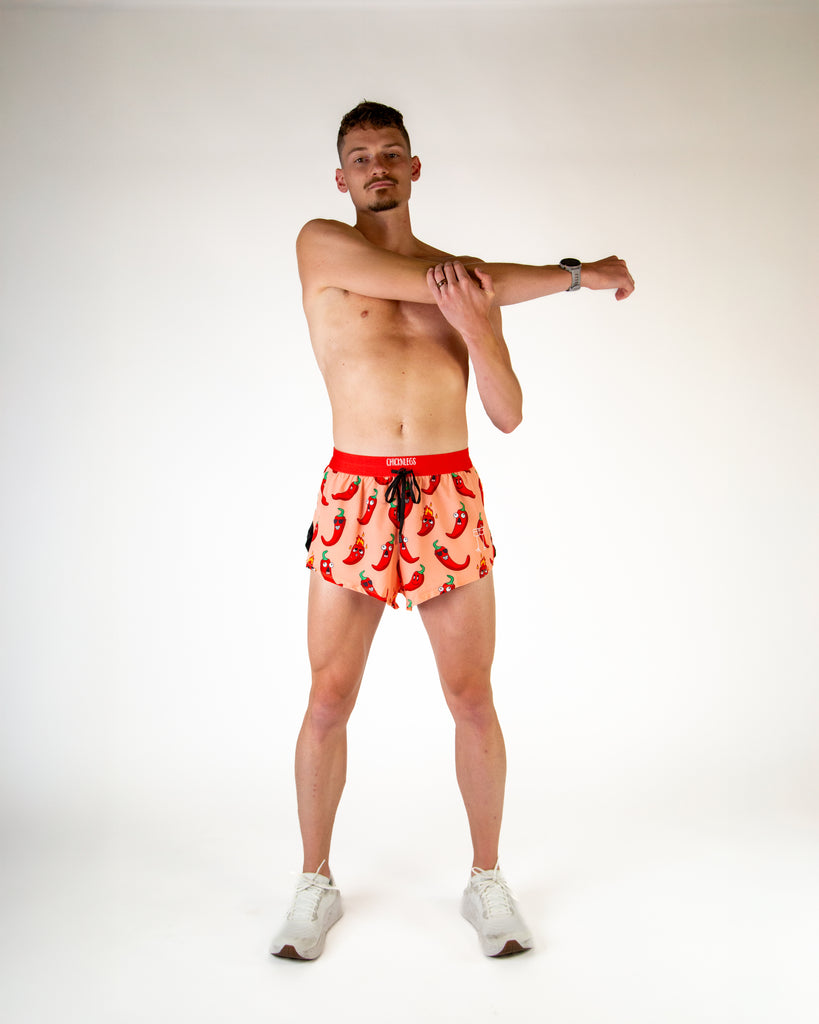 Full body view of model wearing ChicknLegs men’s 2-inch split running shorts in orange with red chili peppers, styled with white running shoes.