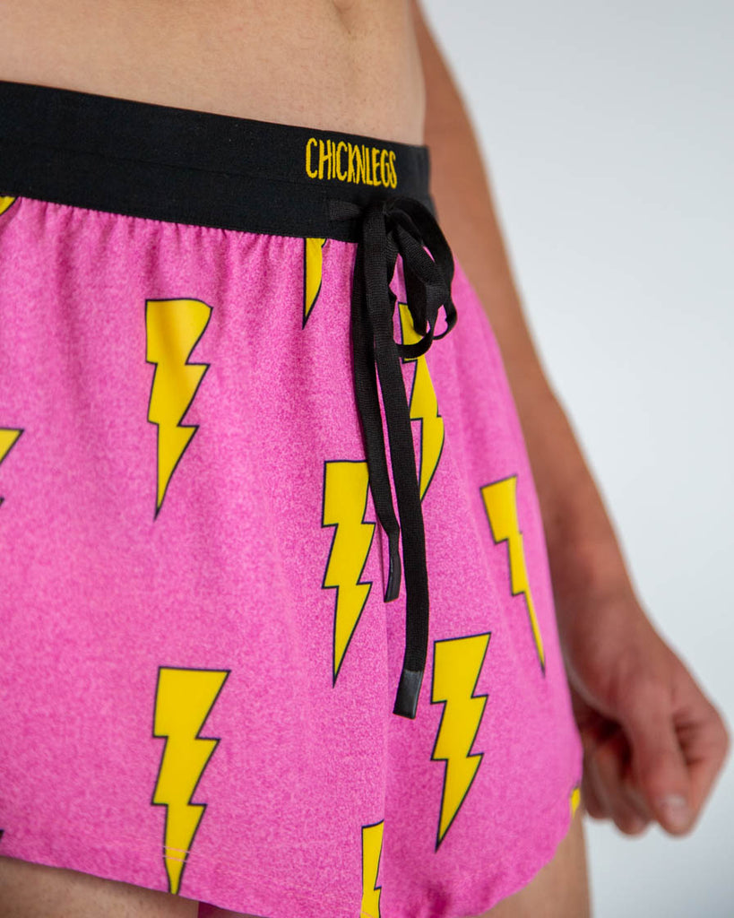Close-up detail of ChicknLegs men’s 2-inch running shorts, hot pink fabric with yellow lightning bolt pattern and drawstring waistband.