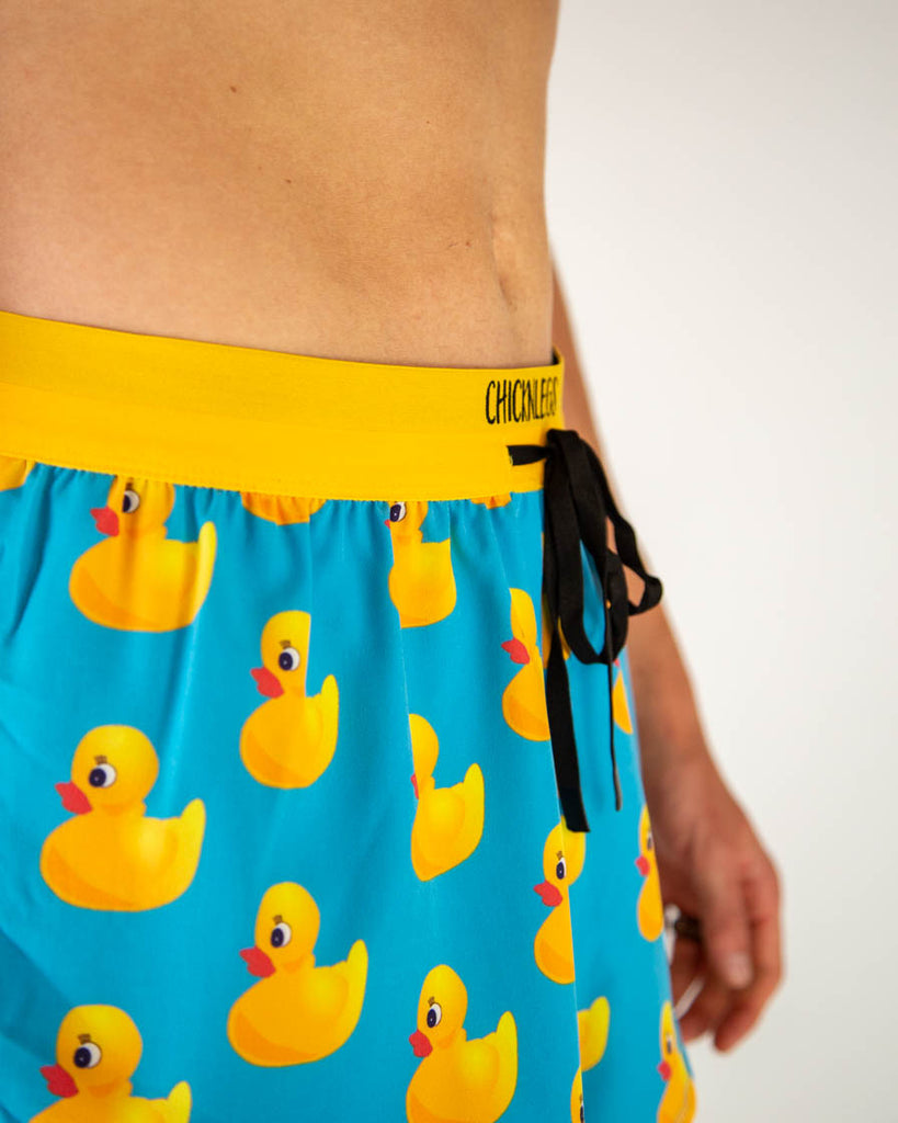 Close-up detail of ChicknLegs men’s 2-inch running shorts, blue fabric with yellow rubbery ducky pattern and yellow drawstring waistband.