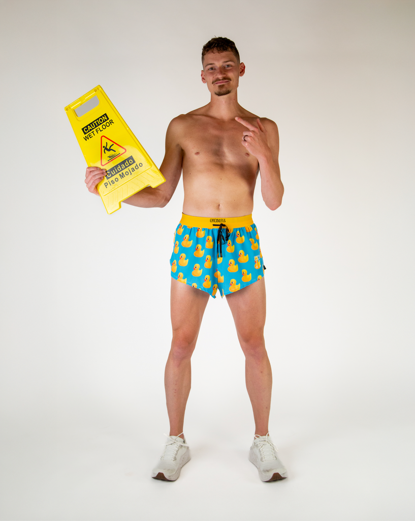 Full body view of model wearing ChicknLegs men’s 2-inch split running shorts in blue with yellow rubber ducky, styled with white running shoes.