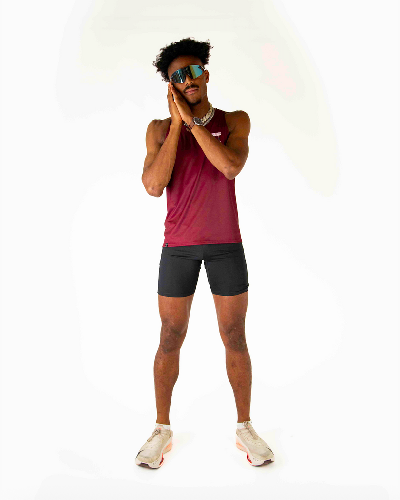 Runner is wearing ChicknLegs in the men's performance singlet in the maroon solid. Model is posing with sunglasses.