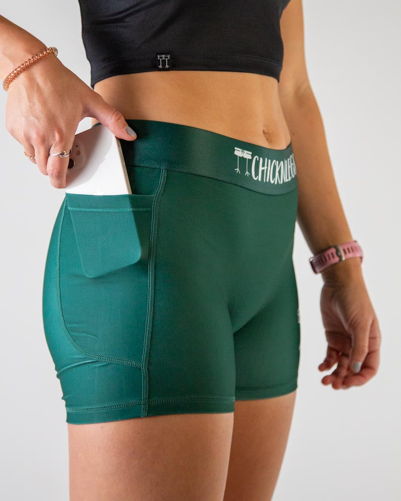A close up image of ChicknLegs women’s 3-inch compression shorts in solid forest green, high-rise waistband, and functional side pocket.