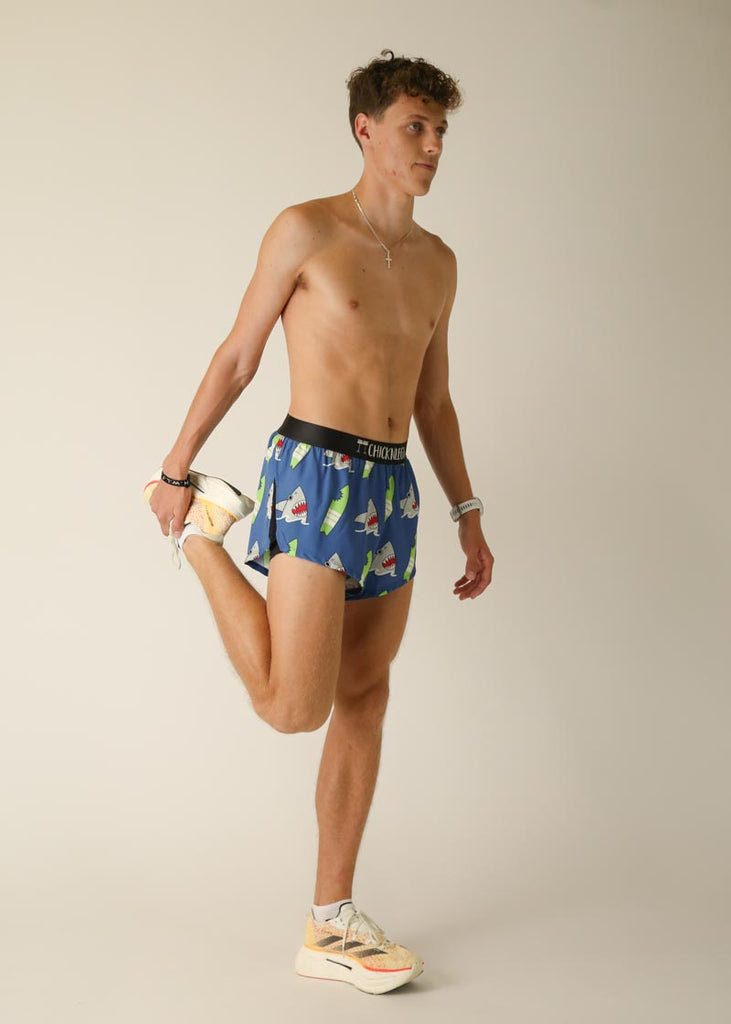 Model wearing Chicknlegs men's 2 inch split running shorts in the blue sharks design, posing while stretching his leg.