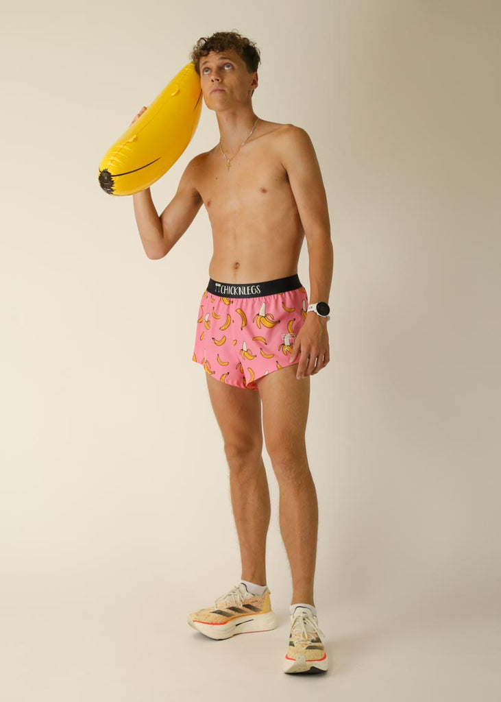 Model wearing Chicknlegs men's 2 inch split running shorts in the pink bananas design, full body view holding a banana and posing as if answering the phone.