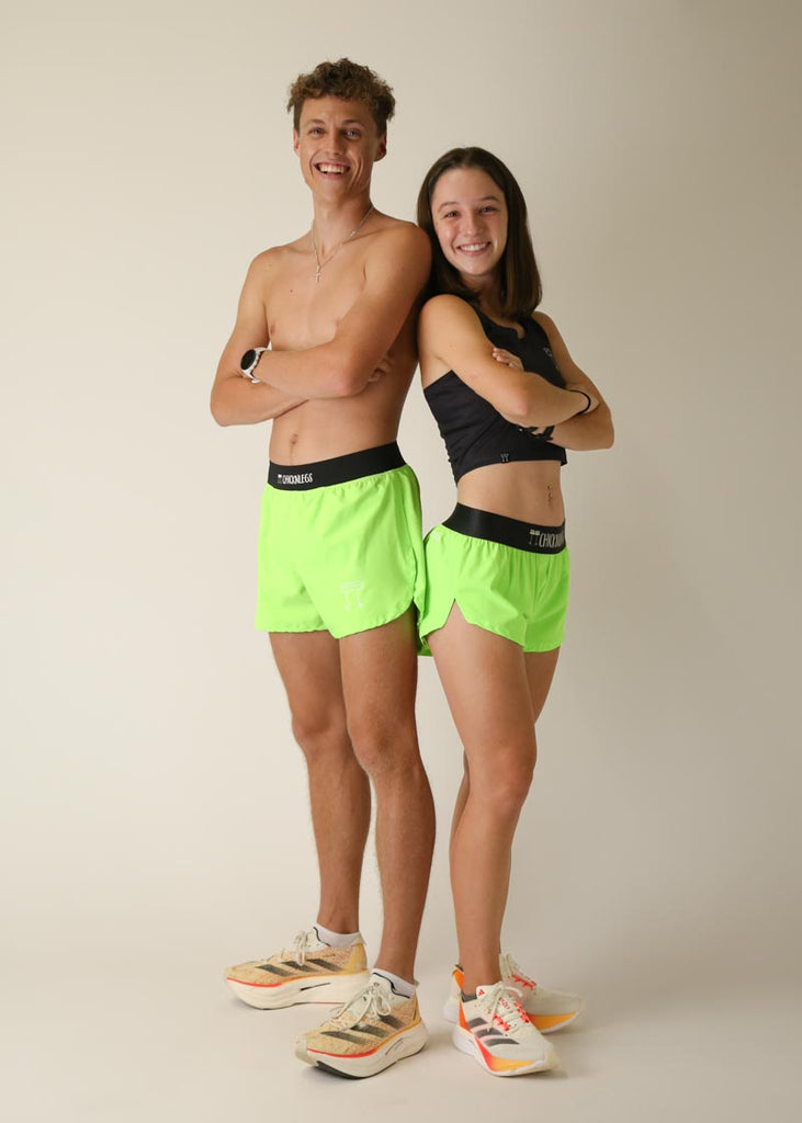 Model wearing Chicknlegs men's 4 inch split running shorts in the neon green design with the women's 1.5 inch split running shorts wearing the neon green design, posing together while crossing their arms.