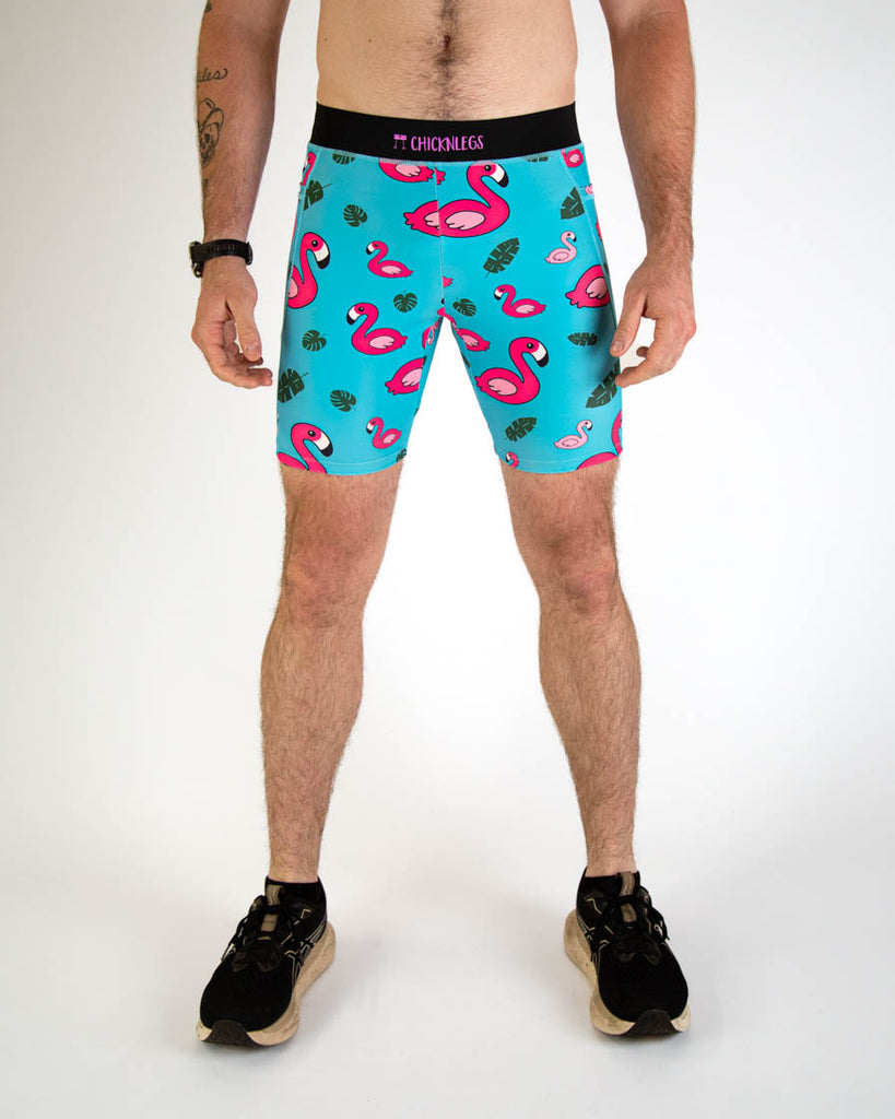 Front view of ChicknLegs men's 8-inch compression spandex running half tights with breathable liner, blue background and pink flamingos, with a black waistband and side pockets.