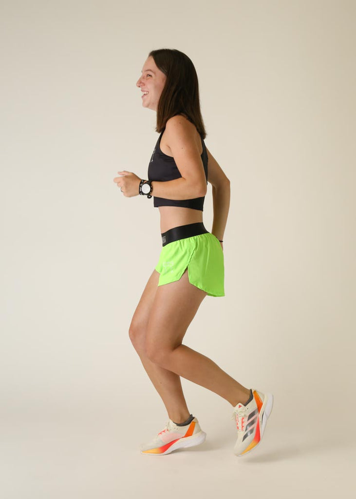 Model wearing Chicknlegs women's 1.5 inch split running shorts in the neon green design in a running pose.
