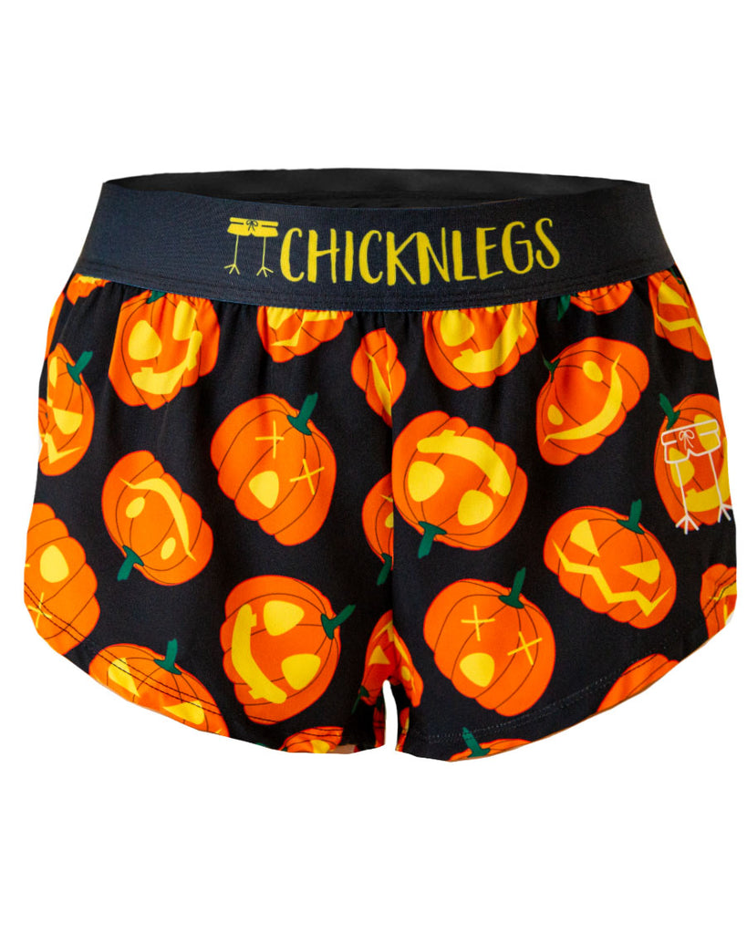 Ghost image of ChicknLegs women's 1.5 inch split running shorts in the pumpkin design. Orange carved jack o lanterns are shown on a black background and black waistband with yellow text.
