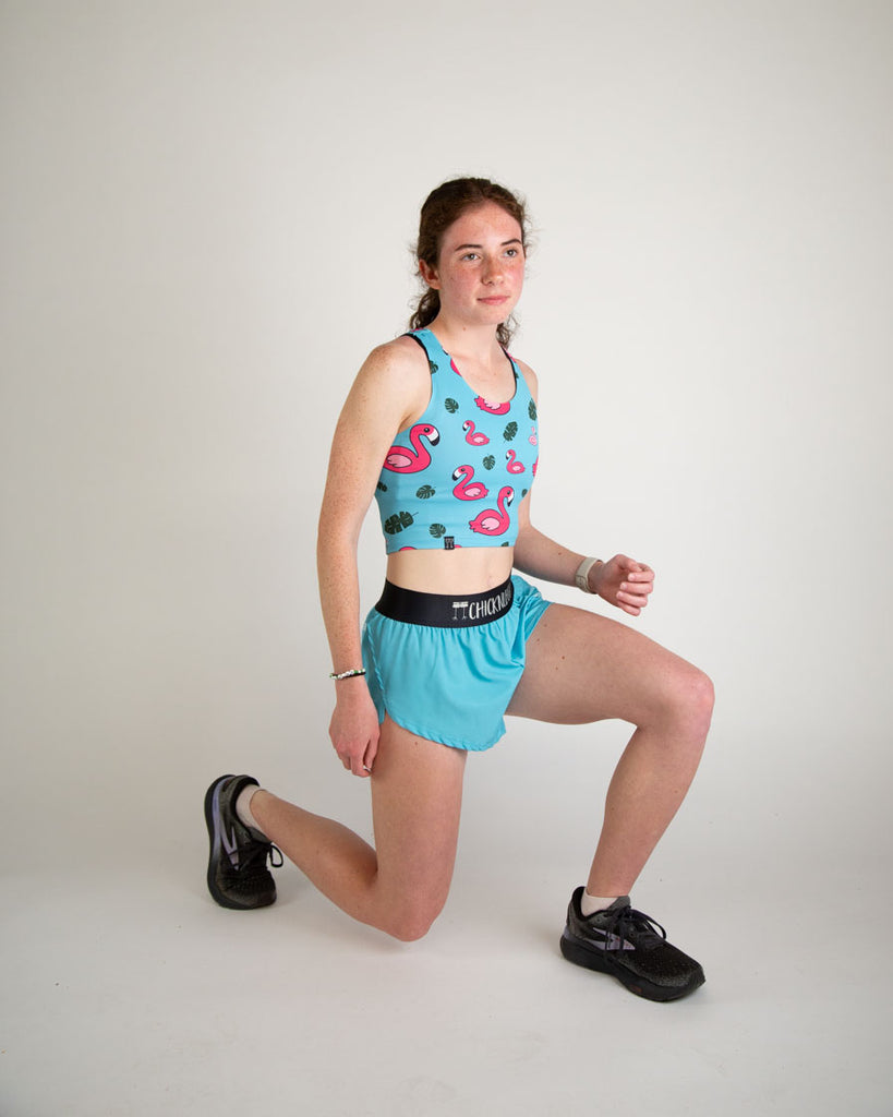 Runner is wearing ChicknLegs in the women's 1.5 in split running shorts in the solid color, sky blue design. Model is stretching to show the flexibility of the shorts with no chaffing.