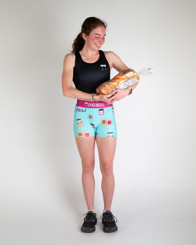 Runner is wearing ChicknLegs in the women's 3 in compression spandex running shorts. The print has blue, brown, purple, and pink on it for the PB&J. Peanut butter and jelly are all around it with stars and toast. Great for people who love food! Model is holding a loaf of bread.