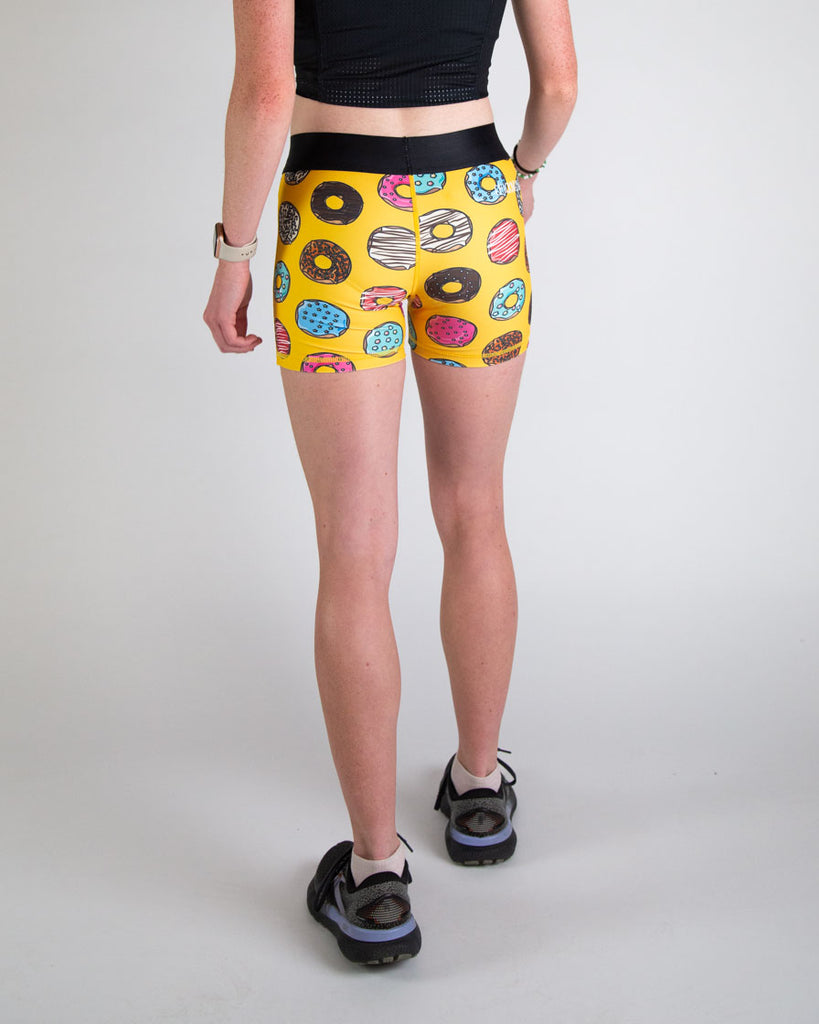 Runner is wearing ChicknLegs in the women's 3 in compression spandex shorts in the salty donuts design. Fun print with food in blue, brown, pink, yellow, red, orange, green, colors! 