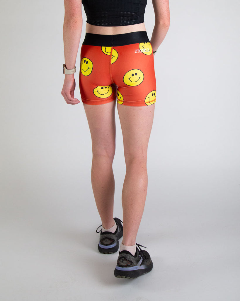 Runner is wearing ChicknLegs in the women's 3 in compression spandex shorts in the smiley print design. The fabric has yellow and orange colors on it with a black waistband. Great for runners with no chaffing and have a soft material. Great for runners who love to smile and have a great time and enjoy the sun.
