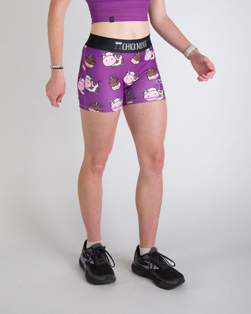 Runner is wearing ChicknLegs in the women's 3 in compression spandex shorts in the choccy cow print. The pattern has chocolate brown cows and chocolate milk on the shorts with a purple background great for matching fits and running.